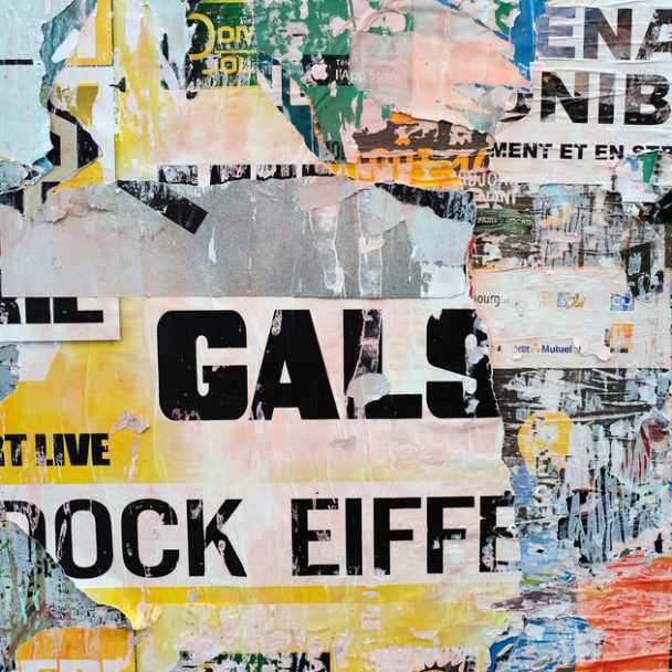 Posters on a grey concrete wall with 'GALS' in large, black letters in the middle